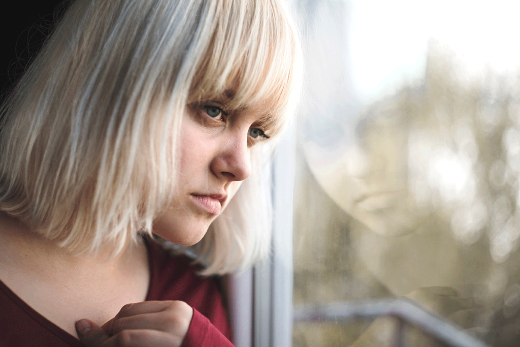 a person looks sadly from a window thinking of commonly abused painkillers