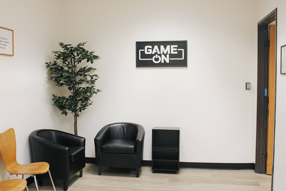 chairs and plants in a lobby area with signs on the walls reading "Game On" and "It's Hard to Beat a PArson Who Never Gives Up"