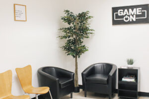 chairs and plants in a lobby area with signs on the walls reading "Game On" and "It's Hard to Beat a PArson Who Never Gives Up"