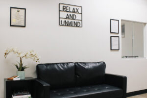 a couch next to an orchid on a shelf with a sign on the wall reading "Relax and Unwind" near a reception window